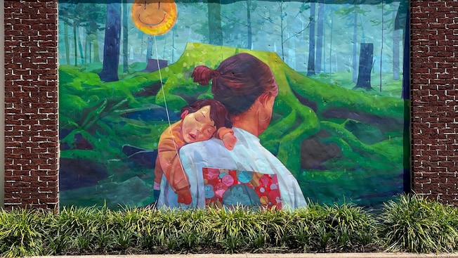 A mural of a mother walking through a forest while she holds her sleeping son 