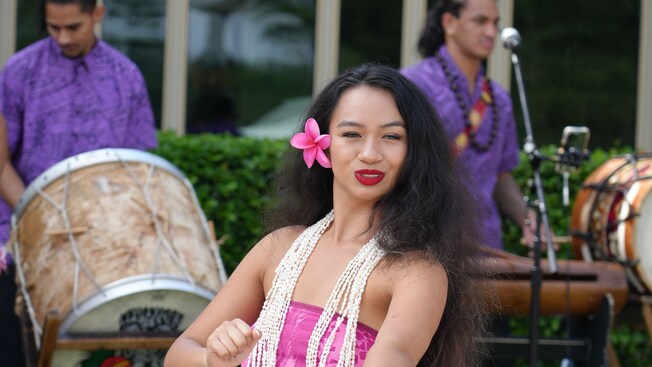 Una bailarina de hula sonriente extendiendo sus brazos durante una actuación en Disney Springs