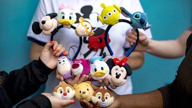 Cuatro personas sosteniendo diademas personalizables con accesorios con personajes de Toy Story, Winnie the Pooh, Lilo & Stitch y algunos Personajes clásicos de Disney