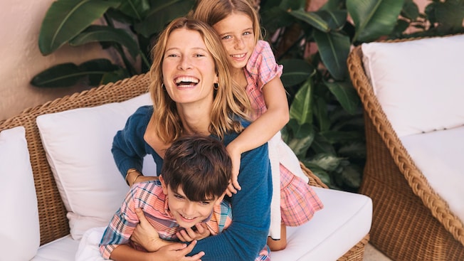 A woman and her 2 kids laughing on a wicker couch