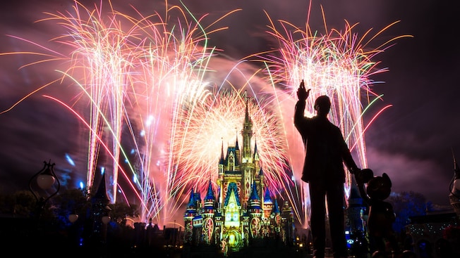Fireworks bursting in the sky over Cinderella Castle and the statue of Walt Disney with Mickey Mouse