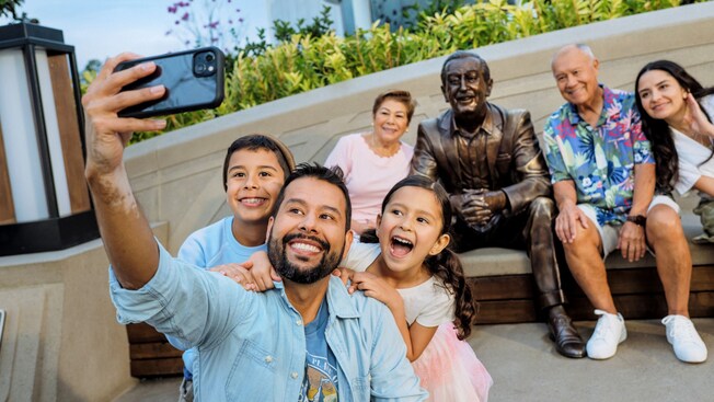 A group of people taking a selfie with the ‘Walt the Dreamer’ statue in World Celebration Gardens