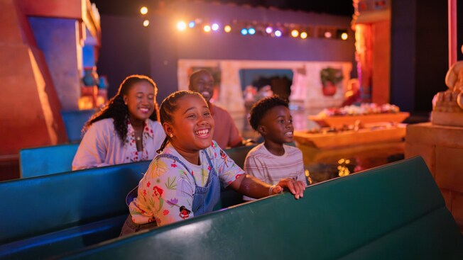 A family of 4 smiling while riding through Gran Fiesta Tour Starring The Three Caballeros