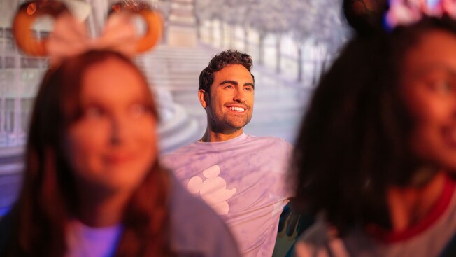 A Guest smiling while seated behind 2 Guests wearing Minnie Mouse ear headbands at Gran Fiesta Tour Starring The Three Caballeros