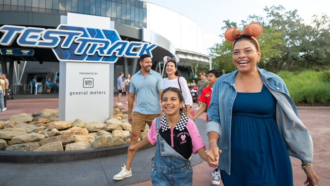 A family of 5 Guests smiling as they walk out of Test Track at Epcot