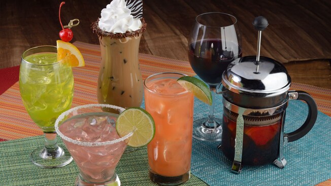 6 bebidas diferentes em uma mesa, incluindo coquetéis, coquetéis sem álcool, uma taça de vinho e uma prensa francesa cheia de café