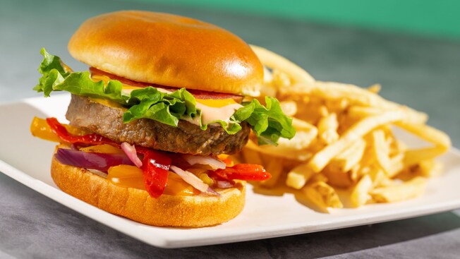 A burger with lettuce, tomato and peppers on a plate with a side of fries