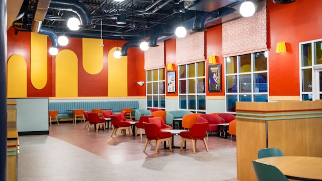 A section of the World Premiere Food Court in Disney's All-Star Movies Resort featuring cushioned chairs, tables and posters of Disney films