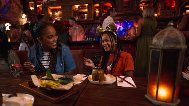 A girl in a Minnie Mouse ear headband laughing with a woman at Beak & Barrel restaurant in Magic Kingdom park