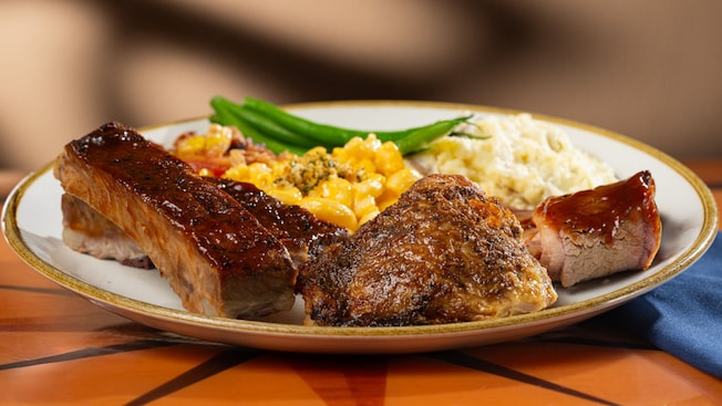 A plate of barbecue ribs and chicken with mashed potatoes and veggies