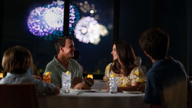 A family sitting at a dining table with a chocolate dessert at California Grill as a fireworks display takes place through the windows behind them
