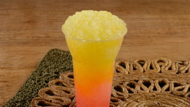 Un vaso grande con hielo raspado de mango y parcha descansa sobre un mantel.