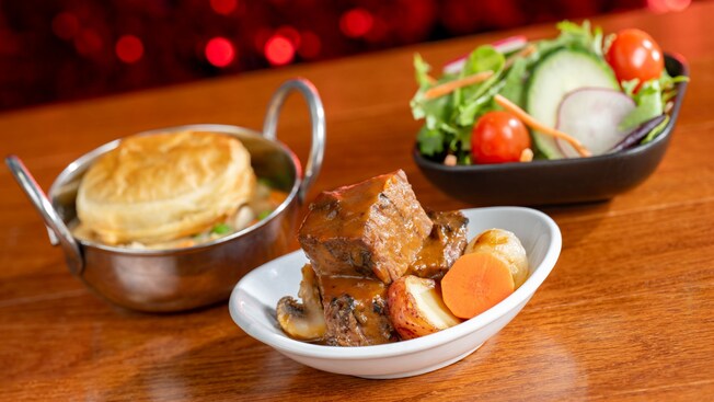 A bowl of pot roast next to chicken pot pie and a salad with vegetables, at Chef Mickey’s