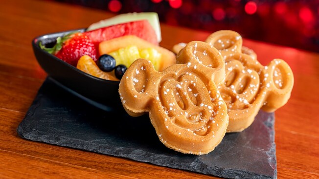 Two Mickey Mouse shaped waffles next to a bowl of fresh fruit, at Chef Mickey’s