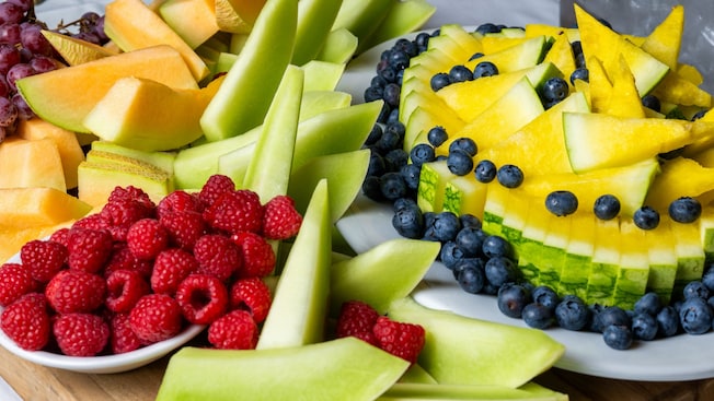 A serving board displaying slices of cantaloupe, honeydew melon, watermelon, raspberries, blueberries and grapes