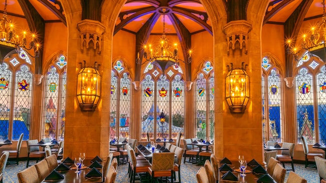 A grand dining room with high arched ceilings, stained glass windows, chandeliers and tables set for Guests