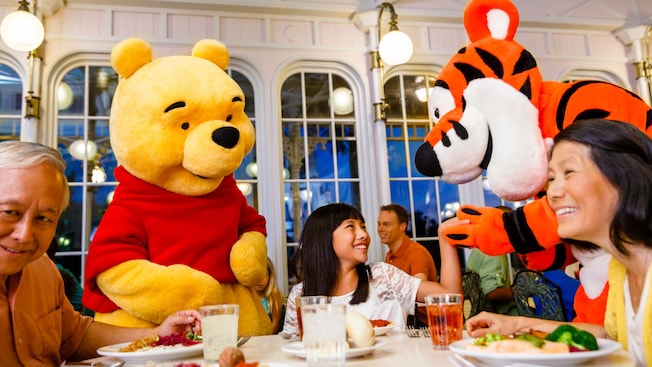 Winnie the Pooh and Tigger greet a family at a table in The Crystal Palace at Magic Kingdom park