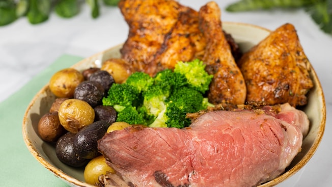 A bowl with roast beef, chicken, broccoli and baby potatoes