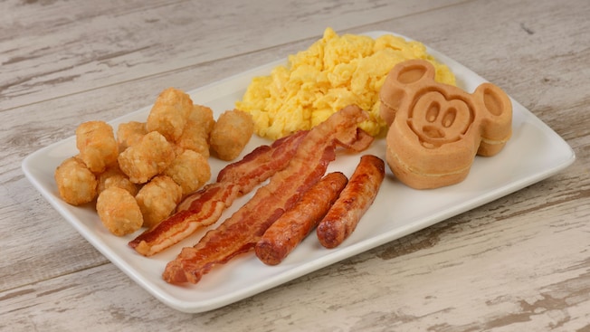 A plate of scrambled eggs, bacon, sausage, hash browns and a Mickey Waffle 