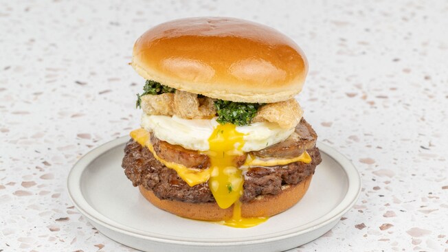 A beef burger topped with porchetta style pork, fried egg, cheese, pork crackling and herbs
