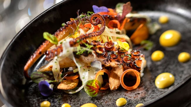 Grilled octopus in a pan surrounded by leafy garnishes