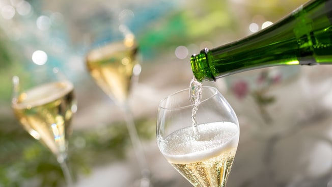 Sparkling wine being poured into 1 of 3 stemmed glasses on a table