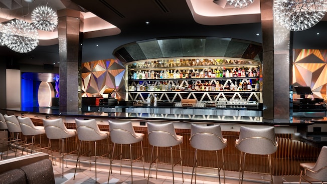 A bar and stools positioned in front of liquor-lined shelves and decor that takes inspiration from the iconic geodesic sphere at EPCOT.