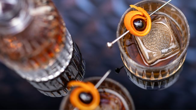 Two Old Fashioned cocktails with orange peel garnish and ice cubes debossed with the shape of Spaceship Earth