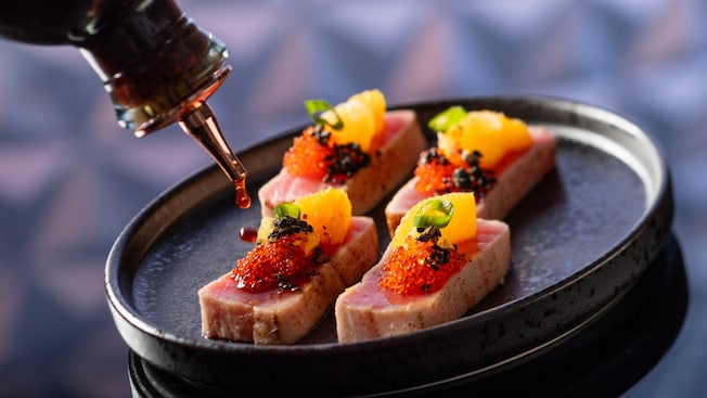 Ahi tuna served in slices topped with orange, fish roe and black sesame seeds drizzled with sauce