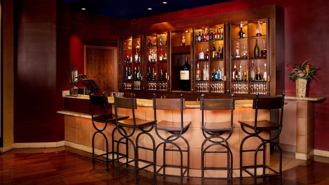 A bar with many bottles of wine, liquor and beer surrounded by barstools