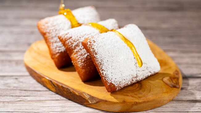 Powdered sugar covered beignets drizzled with honey on a wooden serving board