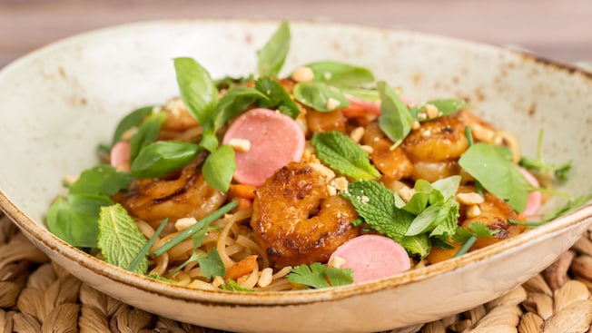 A bowl of rice noodles with sauteed shrimp, pickled radish, eggs, toasted peanuts and herbs