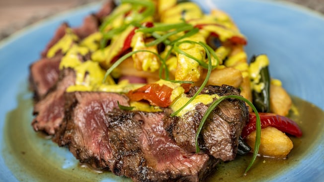 A plate of marinated hanger steak lomo saltado style with roasted peppers, onions, tomatoes and aji amarillo aioli