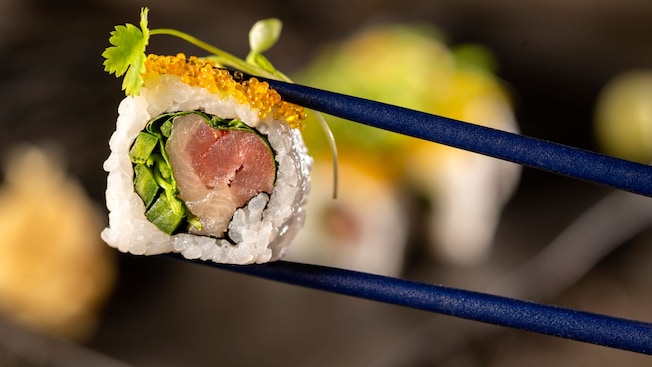 A piece of sushi held between a pair of chopsticks