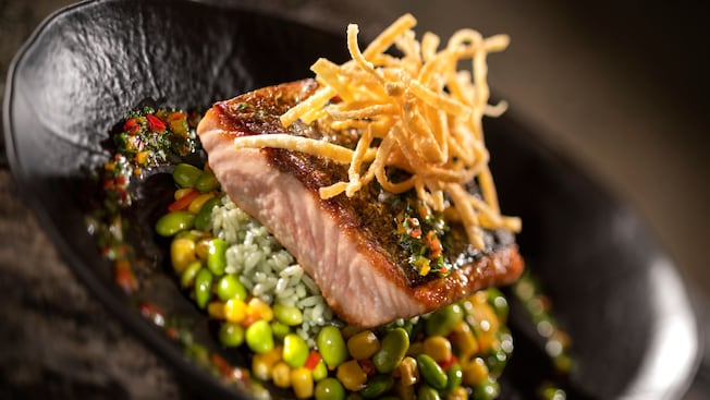 A plate containing cooked salmon, rice and vegetables topped with crispy noodles