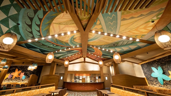 A room with Polynesian inspired decorations including a ceiling mural and plumeria flower carvings