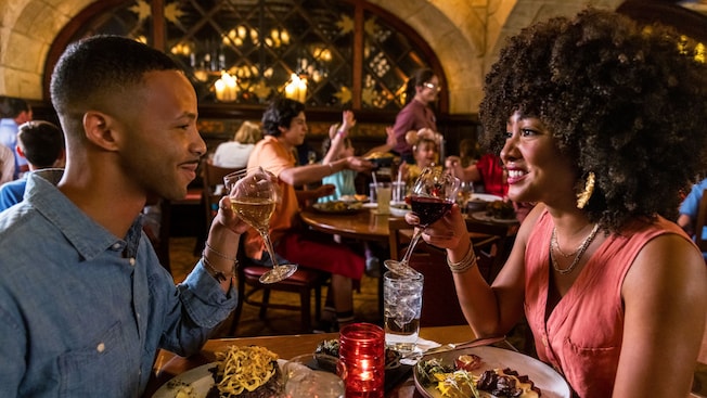 Un homme et une femme savourent un souper aux chandelles, des verres à vin serrés et sourient au Cellier Steakhouse