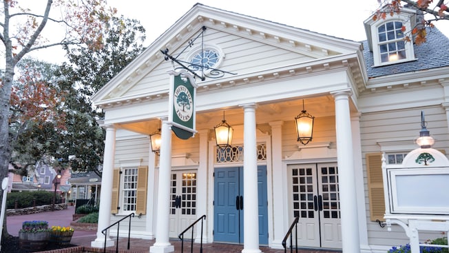 Un edificio estilo colonial con cuatro columnas, faroles colgantes, tres juegos de puertas dobles y un letrero que dice ‘Liberty Tree Tavern’