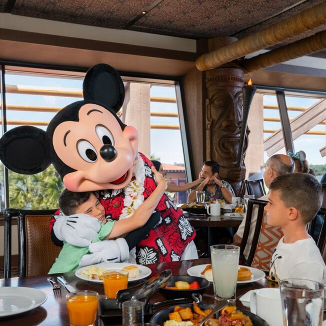 Two boys at a table hugging Mickey Mouse and having breakfast at 'Ohana
