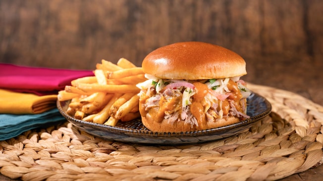A Smoked Pork Sandwich topped with coleslaw and sauce served with French fries on a plate