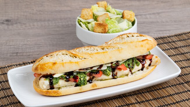 Chicken Caprese Baguette Sandwich with pesto and balsamic drizzle alongside a Caesar Salad