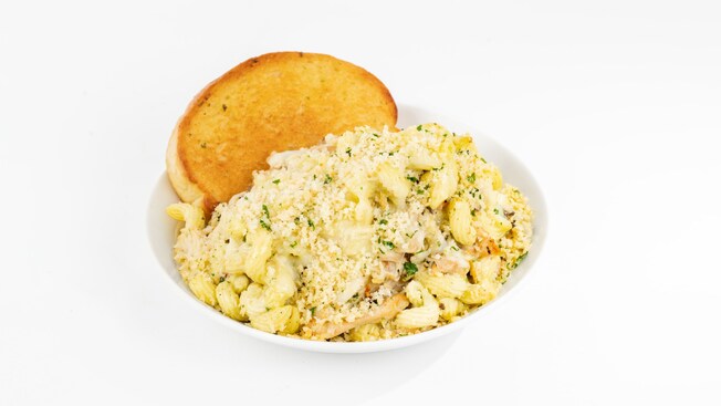 Bowl of Creamy Pesto Chicken Pasta topped with Parmesan cheese and served with garlic bread