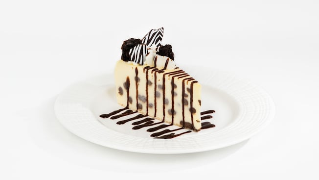 Slice of Marbled Swirled Cheesecake drizzled with chocolate sauce and topped with whipped cream and mini brownies