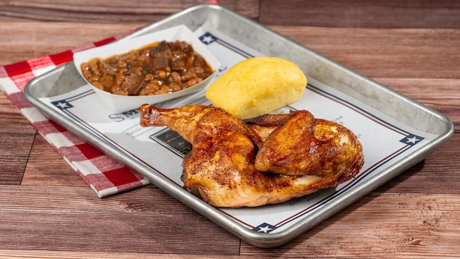 Medio pollo rostizado servido con frijoles horneados y un muffin de pan de maíz en una bandeja