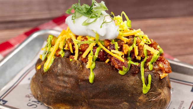 Una papa alargada horneada cubierta con abundante chile, queso, sour cream y salsa de aguacate