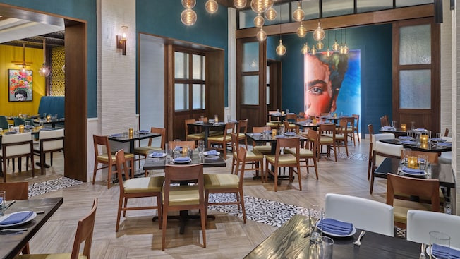 Dois salões de jantar, ambos com decoração moderna e quadros na parede representando a artista Frida Kahlo