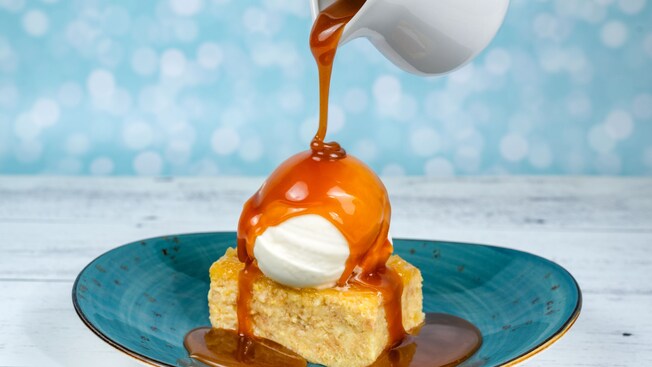 Coconut pineapple bread pudding with caramel sauce being poured from a pitcher over a dollop of cream from Sebastian's Bistro