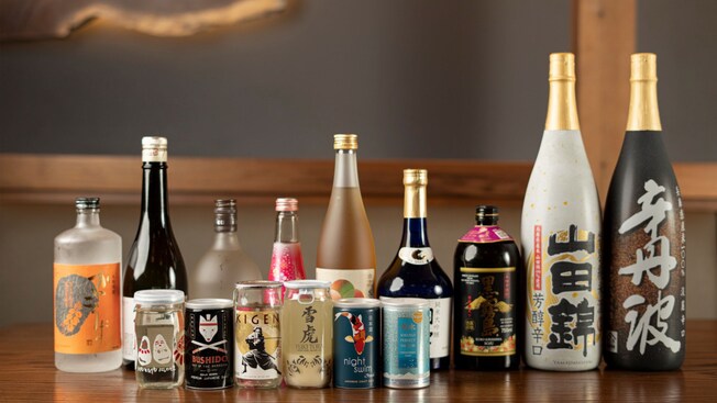 Many bottles and cans of sake lined up on a counter