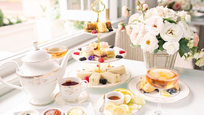 An elegant set up for afternoon tea featuring a tea pot, finger sandwiches, mini desserts and a cocktail