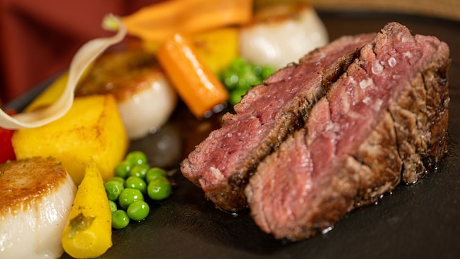 A plated dish featuring grilled beef tenderloin with seared scallops, potatoes and vegetables